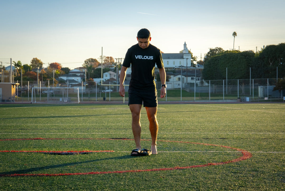 Man stepping into black VELOUS Hoya Adjustable Slides on a sports field after training