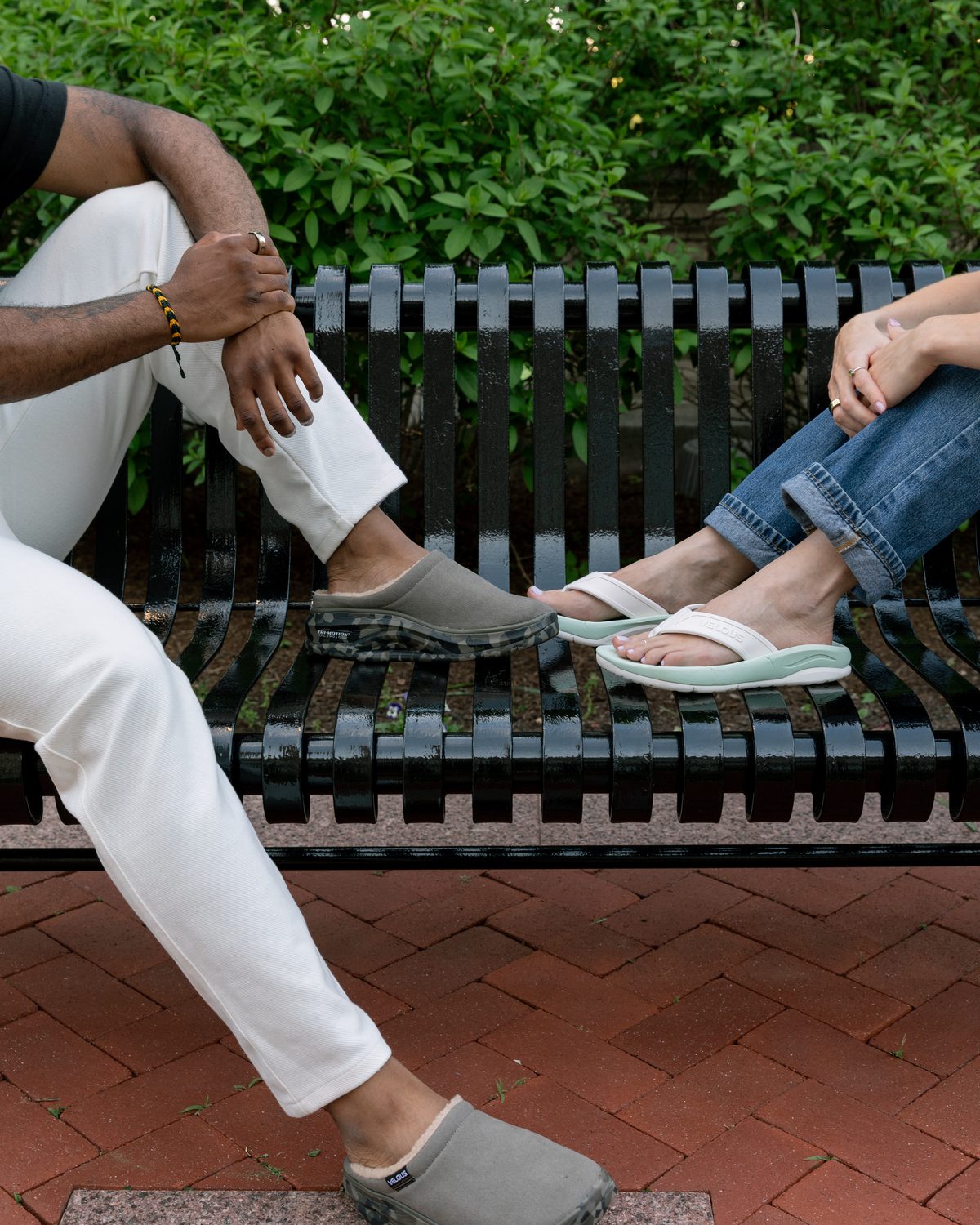 Two people seated on a bench wearing VELOUS recovery footwear